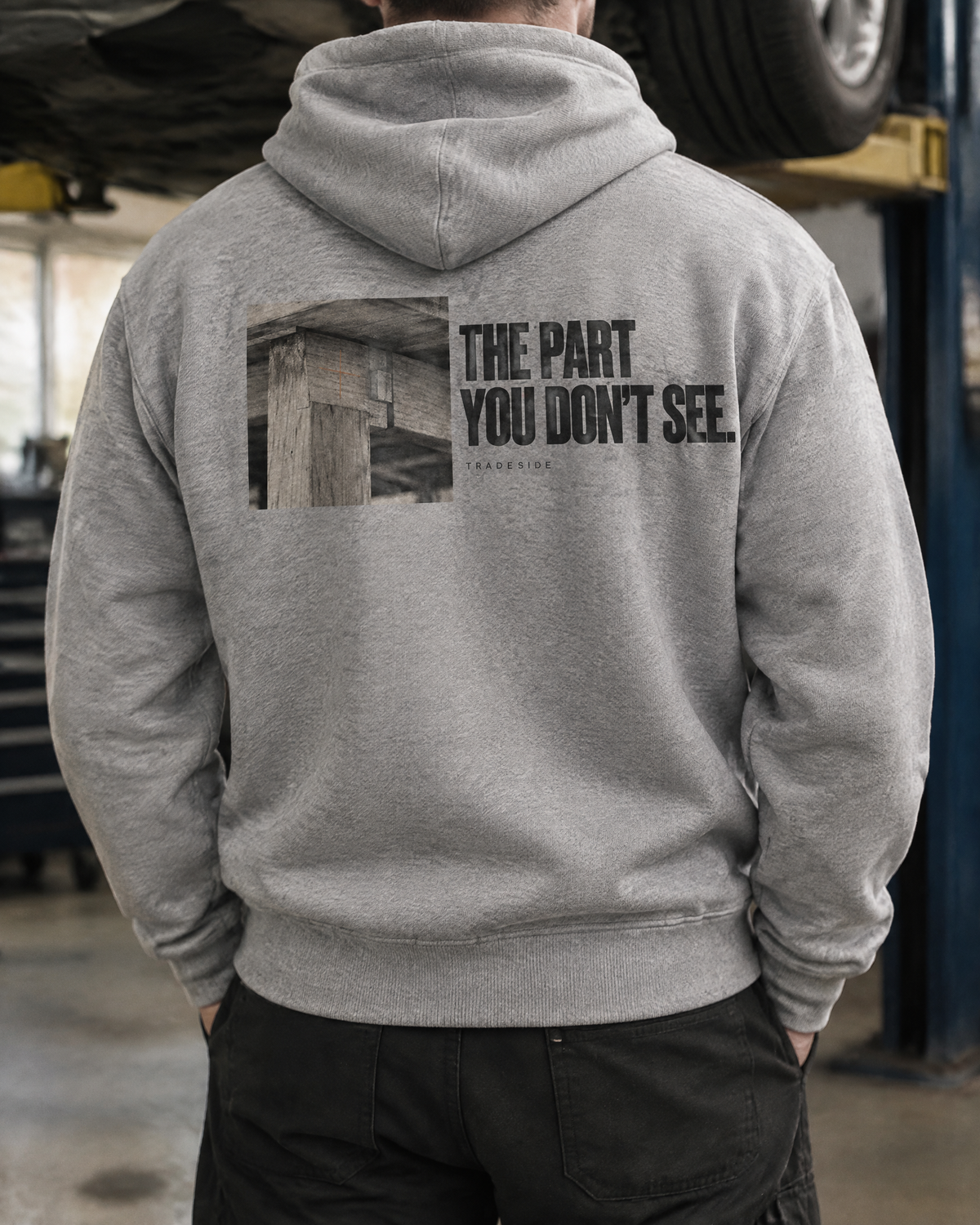 The Part You Don't See hoodie, back print, worn by a mechanic in a garage